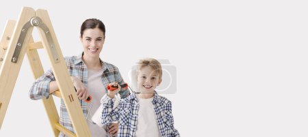 Foto de Feliz joven mujer y niño sosteniendo un rodillo de pintura, que están pintando y decorando su casa, pancarta con espacio para copias - Imagen libre de derechos