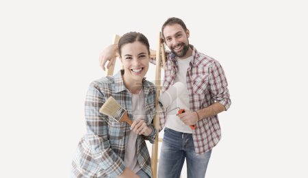 Téléchargez les photos : Jeune couple créatif rénovant leur maison et peignant des murs, ils posent ensemble et sourient à la caméra - en image libre de droit