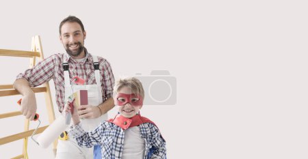 Téléchargez les photos : Peintre professionnel confiant et super-héros garçon peignant une maison ensemble, relooking à la maison et concept de décoration - en image libre de droit