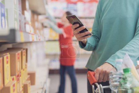 Frau mit Smartphone im Supermarkt beim Einkaufen, Hände aus nächster Nähe