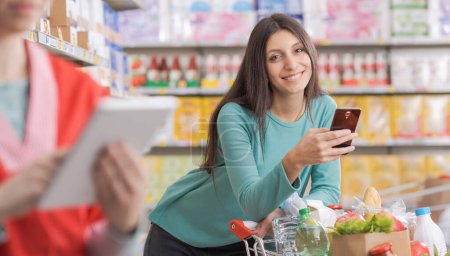 Junge Frau mit Smartphone im Supermarkt und lächelt in Kamera