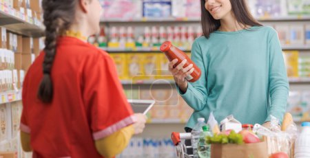 Téléchargez les photos : Employé amical de l'épicerie aidant une femme, le client sourit et tient un produit - en image libre de droit