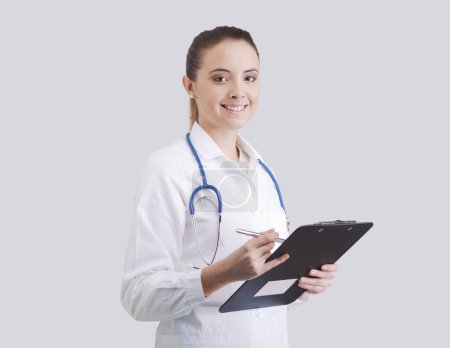 Photo for Portrait of a young female doctor smiling at camera and holding a clipboard, medical assistance and healthcare concept - Royalty Free Image