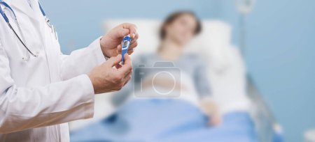 Téléchargez les photos : Médecin prenant la température d'un patient à l'aide d'un thermomètre numérique, le patient est allongé sur le lit - en image libre de droit