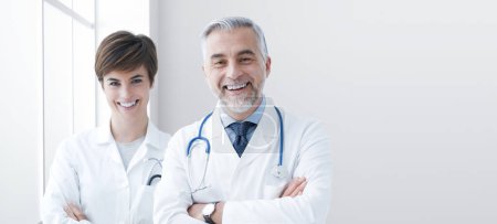 Téléchargez les photos : Médecins confiants posant et souriant à la caméra, intérieur de la chambre d'hôpital en arrière-plan - en image libre de droit