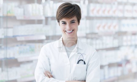 Téléchargez les photos : Jeune pharmacien professionnel posant les bras croisés et souriant, intérieur de magasin en arrière-plan - en image libre de droit
