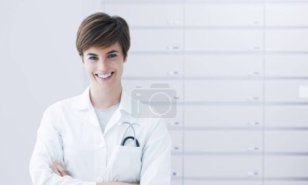 Photo for Professional female pharmacist posing in front on pharmacy drawers - Royalty Free Image