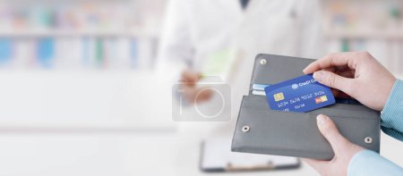 Téléchargez les photos : Femme achetant des médicaments sur ordonnance dans la pharmacie, elle prend la carte de crédit du portefeuille - en image libre de droit