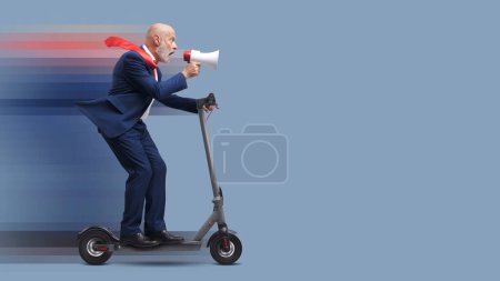 Foto de Hombre de negocios corporativo senior montando un scooter eléctrico rápido y gritando a través de un megáfono - Imagen libre de derechos
