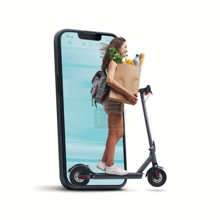 Téléchargez les photos : Femme tenant un sac en papier avec épicerie et conduisant un scooter électrique, elle sort d'un écran de smartphone, concept d'épicerie en ligne - en image libre de droit