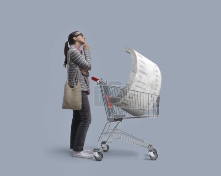 Photo for Worried indecisive customer thinking and big heavy grocery receipt in a shopping cart: inflation, prices rise and budgeting concept - Royalty Free Image
