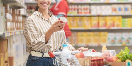 Téléchargez les photos : Femme heureuse tenant une canette et lisant une étiquette de la valeur nutritive au supermarché, épicerie et concept de nutrition - en image libre de droit