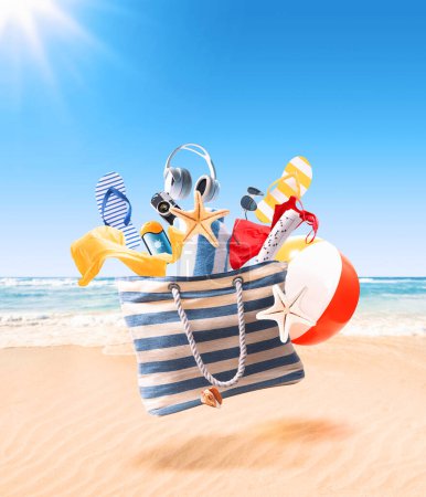 Foto de Bolso de playa volador, accesorios coloridos que caen y playa de arena en el fondo: concepto de vacaciones de verano - Imagen libre de derechos