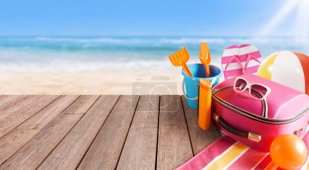 Téléchargez les photos : Sac de voyage, accessoires colorés sur le pont de la plage et la mer en arrière-plan : vacances d'été et concept de voyage - en image libre de droit