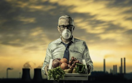 Businessman with protective mask holding a crate with polluted poisonous vegetables, food pollution concept