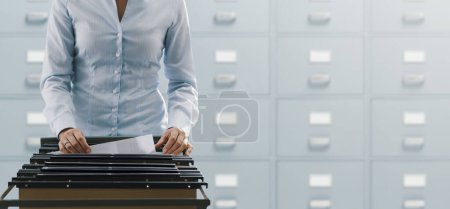Büroangestellte durchsucht Akten und Unterlagen im Archiv, sie prüft Ordner in einem Aktenschrank