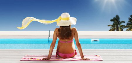 Young beautiful woman sunbathing at the tropical resort, she is relaxing at the swimming pool, summer vacations concept