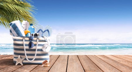 Téléchargez les photos : Sac de plage avec accessoires sur la promenade de plage à la station tropicale, océan en arrière-plan, voyage et vacances d'été concept - en image libre de droit