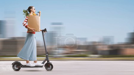 Young woman carrying a paper bag with groceries and riding a fast electric scooter, grocery shopping concept