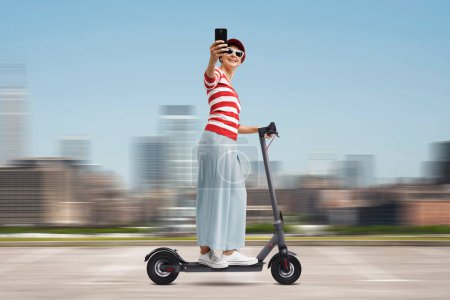 Foto de Mujer distraída montando un scooter eléctrico en la calle y usando su teléfono inteligente - Imagen libre de derechos