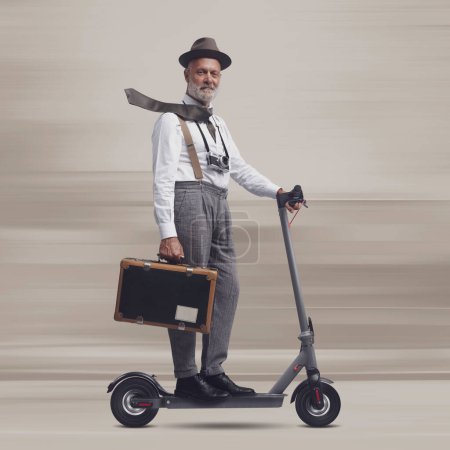 Photo for Vintage style man carrying a suitcase and riding an electric scooter, he is a traveler and photographer - Royalty Free Image