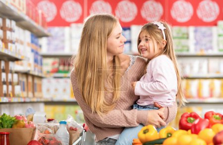 Foto de Retrato de una madre feliz sosteniendo a su hija en la tienda de comestibles, que están sonriendo el uno al otro, compras de comestibles y el concepto de estilo de vida - Imagen libre de derechos