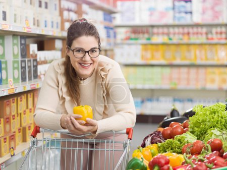 Téléchargez les photos : Femme souriante poussant un panier et achetant des légumes frais et sains au supermarché, épicerie et concept de nutrition - en image libre de droit