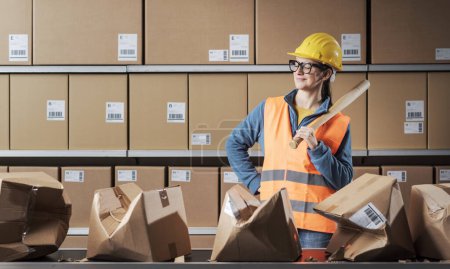 Photo for Confident smiling rebellious worker posing with a baseball bat at the warehouse, she is angry and she smashed many cardboard boxes - Royalty Free Image