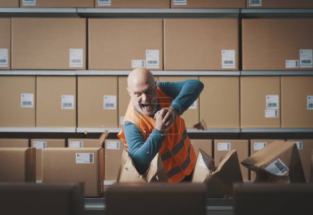 Photo for Furious rebellious worker tearing boxes at the warehouse and screaming, he is angry and frustrated - Royalty Free Image