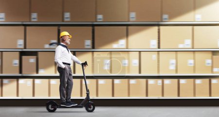 Photo for Distribution warehouse manager wearing a safety helmet and riding an electric scooter - Royalty Free Image