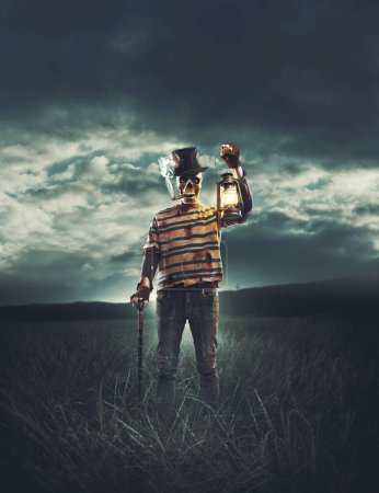 Téléchargez les photos : Mal caractère effrayant avec tête de crâne debout dans les champs et tenant une lanterne - en image libre de droit