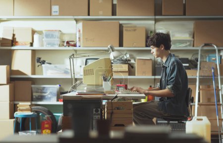 Foto de Joven empollón sentado en el escritorio y trabajando con una computadora vintage en su garaje - Imagen libre de derechos