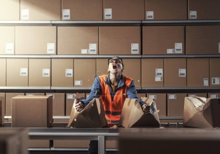 Photo for Angry rebellious worker punching and smashing boxes on the conveyor belt in the warehouse, she is frustrated and furious - Royalty Free Image