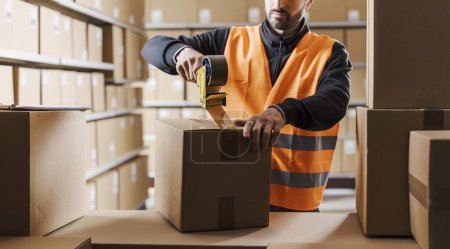 Warehouse worker sealing a cardboard box with adhesive tape, logistics and shipment concept