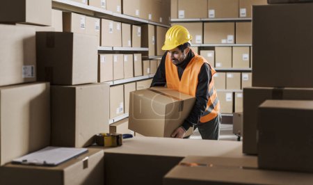 Photo for Tired warehouse worker having a bad back pain at work, he is lifting a big heavy box - Royalty Free Image