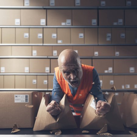 Photo for Furious rebellious worker crushing boxes at the warehouse and screaming, he is angry and frustrated - Royalty Free Image