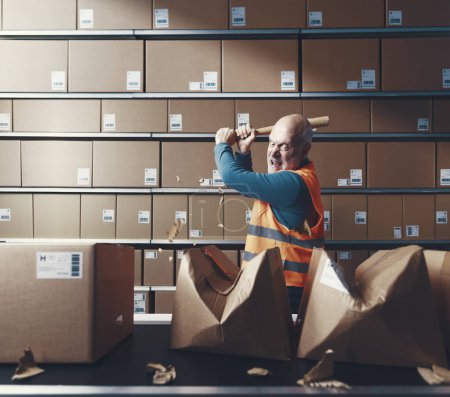 Photo for Crazy rebellious warehouse worker smashing cardboard boxes with a baseball bat - Royalty Free Image