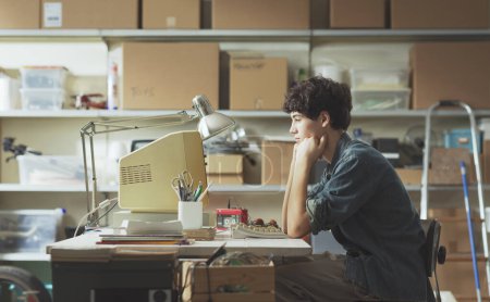 Téléchargez les photos : Adolescent intelligent concentré assis au bureau dans son garage et travaillant avec un ordinateur vintage - en image libre de droit
