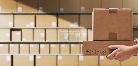 Trabajador de almacén sosteniendo cajas de entrega y paquetes apilados en segundo plano, logística y concepto de envío