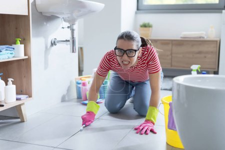Foto de Mujer obsesionada enojada limpiando el piso del baño usando un cepillo de dientes - Imagen libre de derechos