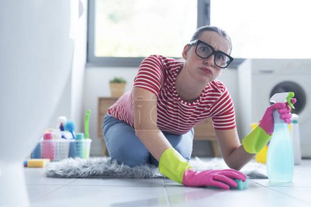 Foto de Mujer haciendo tareas en casa, ella está arrodillada en el suelo y limpiando las baldosas con una esponja - Imagen libre de derechos