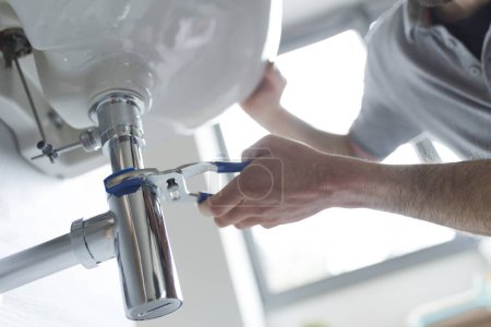 Plombier professionnel réparant un évier de salle de bain qui fuit, il utilise des pinces à pompe à eau