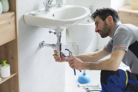 Plombier vérifiant un drain d'évier de salle de bains et utilisant des pinces de pompe à eau