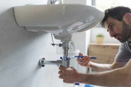 plombier professionnel fixant un lavabo de salle de bains, il utilise des pinces à pompe à eau