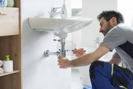 Plombier professionnel fixant un drain d'évier de salle de bains à l'aide de pinces à pompe à eau