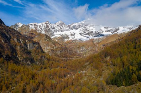 Téléchargez les photos : Montagnes enneigées avec forêt dans un pré sous un ciel nuageux - en image libre de droit