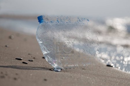 Téléchargez les photos : Le problème de la micro pollution plastique, image conceptuelle. Bouteille en plastique sur la plage absorbée par l'océan. - en image libre de droit