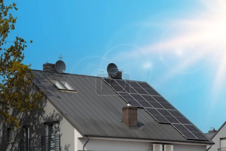 Téléchargez les photos : Maison élégante avec panneaux photovoltaïques sombres, temps ensoleillé - en image libre de droit