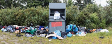 Clothing Donation Overflow. Overflowing donation bin with scattered clothes in a natural setting.