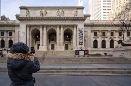 Téléchargez les photos : Une touriste saisit l'essence de New York, photographiant la bibliothèque publique emblématique avec son smartphone. - en image libre de droit